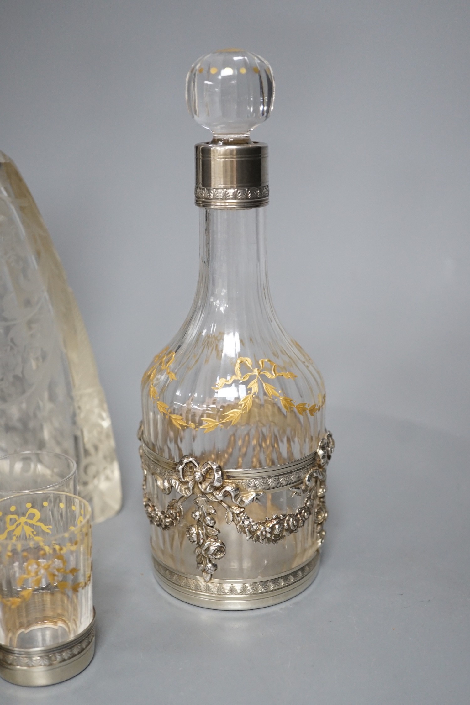 An early 20th century French white metal mounted gilded glass decanter and stopper and four matching tots, decanter height 19.7cm, and a French white metal collared etched glass decanter and stopper.